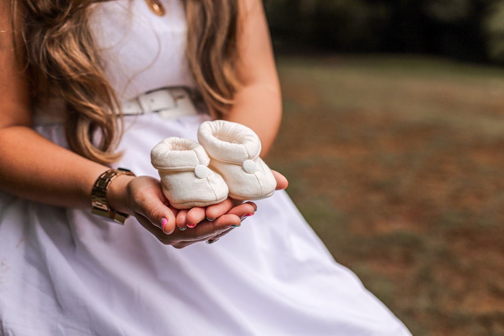 a little girl in a white dress holding two baby shoes