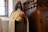 A statue of a woman dressed in a religious habit holding a bouquet of yellow and pink roses, standing next to a wooden confessional booth in a church setting with stained glass windows.