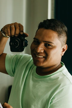 Close-up shot of a smiling artist holding a camera in natural light.