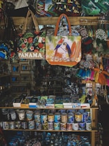 A vibrant souvenir shop display featuring a variety of colorful items including Panama-themed bags, mugs, and decorative objects. The bags showcase designs with tropical birds and floral patterns. Mugs arranged neatly on shelves display various prints, and there are dreamcatchers and other trinkets hanging on the side.