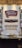 A bar with a white tile backsplash features multiple beer taps lined up in a neat row. Above the taps are signage for Lansing Brewing Company and Hard Nose Spirits. Shelves on either side hold bottles, and a wooden ceiling adds a rustic touch.