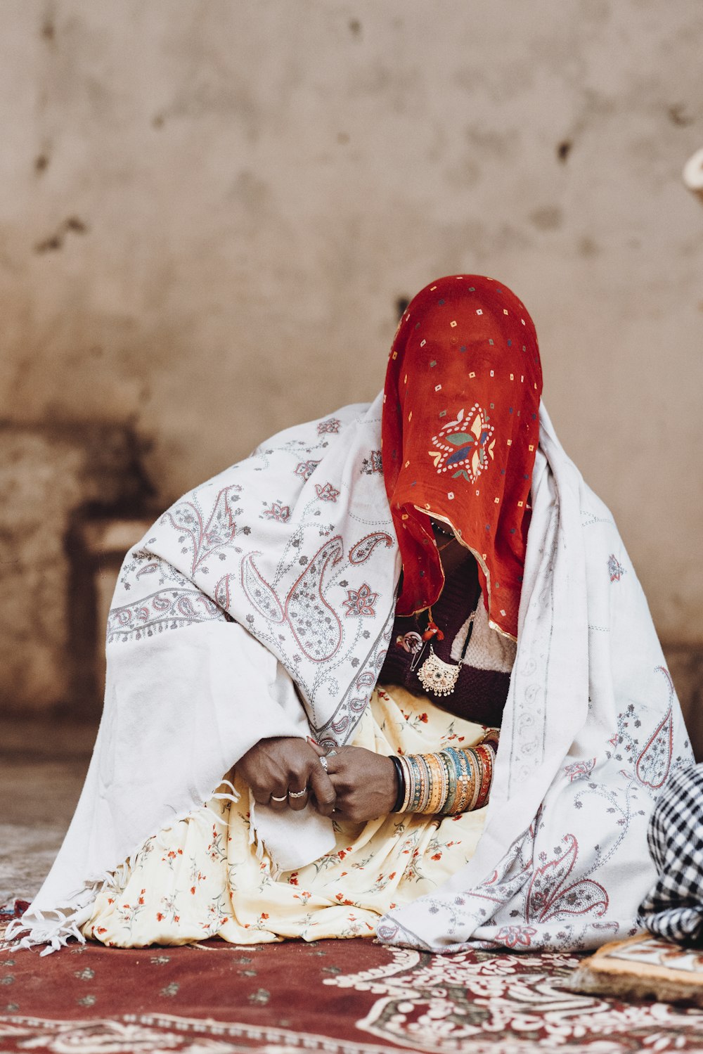 a woman sitting on the ground wearing a red head scarf