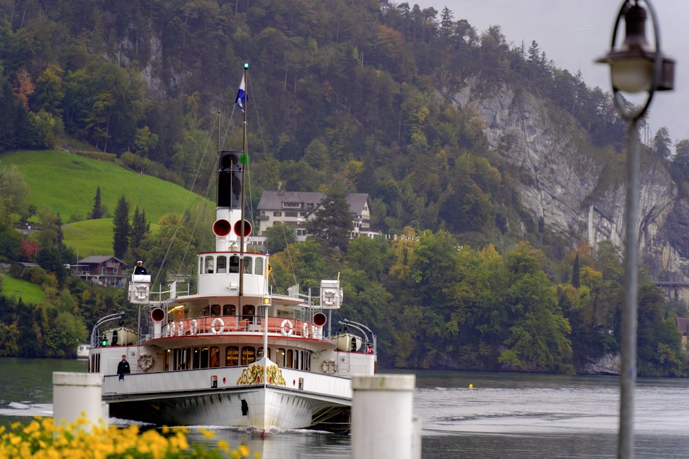 a large boat floating on top of a lake next to a lush green hillside