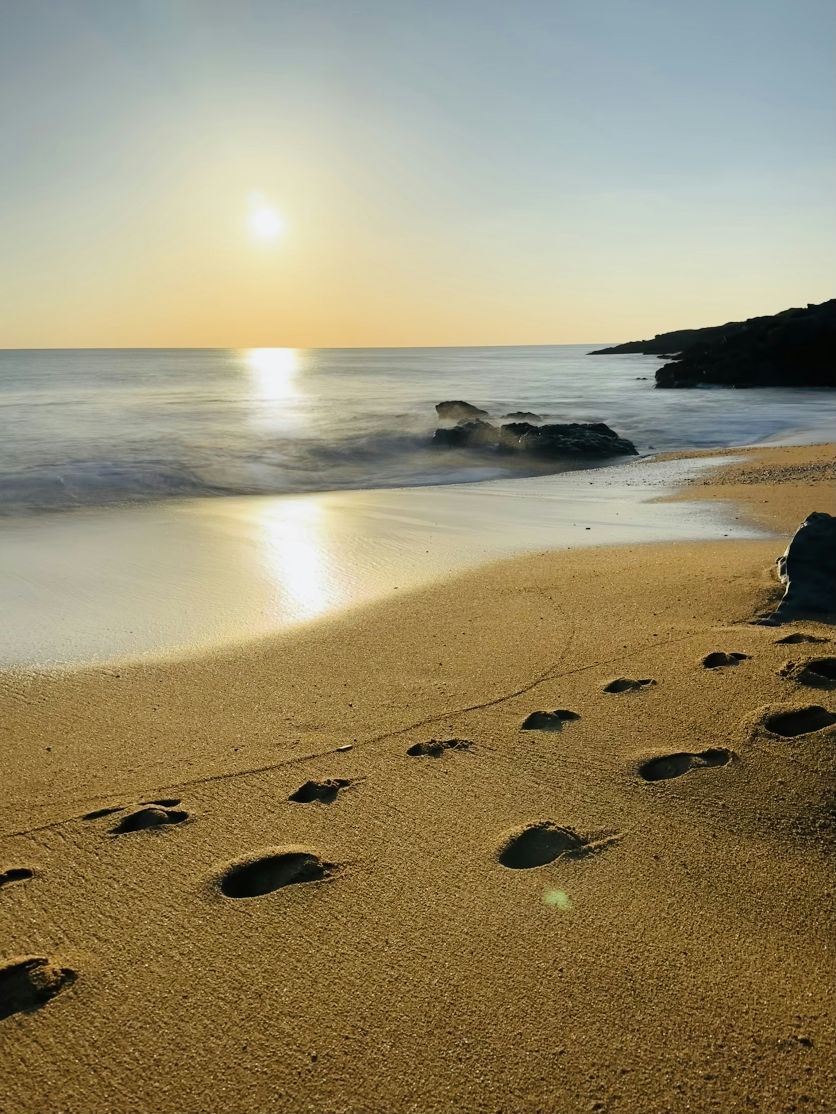Une plage avec des empreintes dans le sable et le soleil en arrière-plan