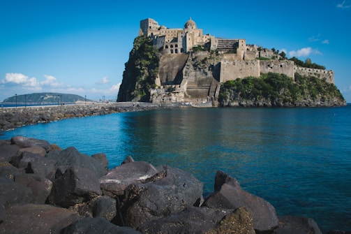 a large castle sitting on top of a mountain next to a body of water