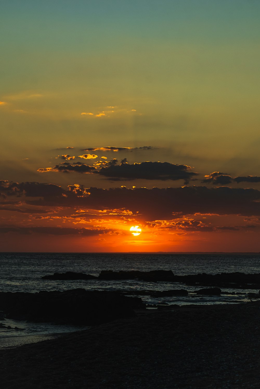 the sun is setting over the ocean on a cloudy day