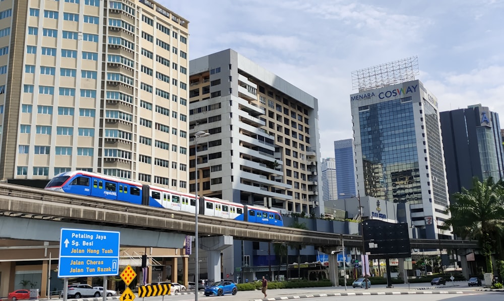 a blue and white train traveling past tall buildings