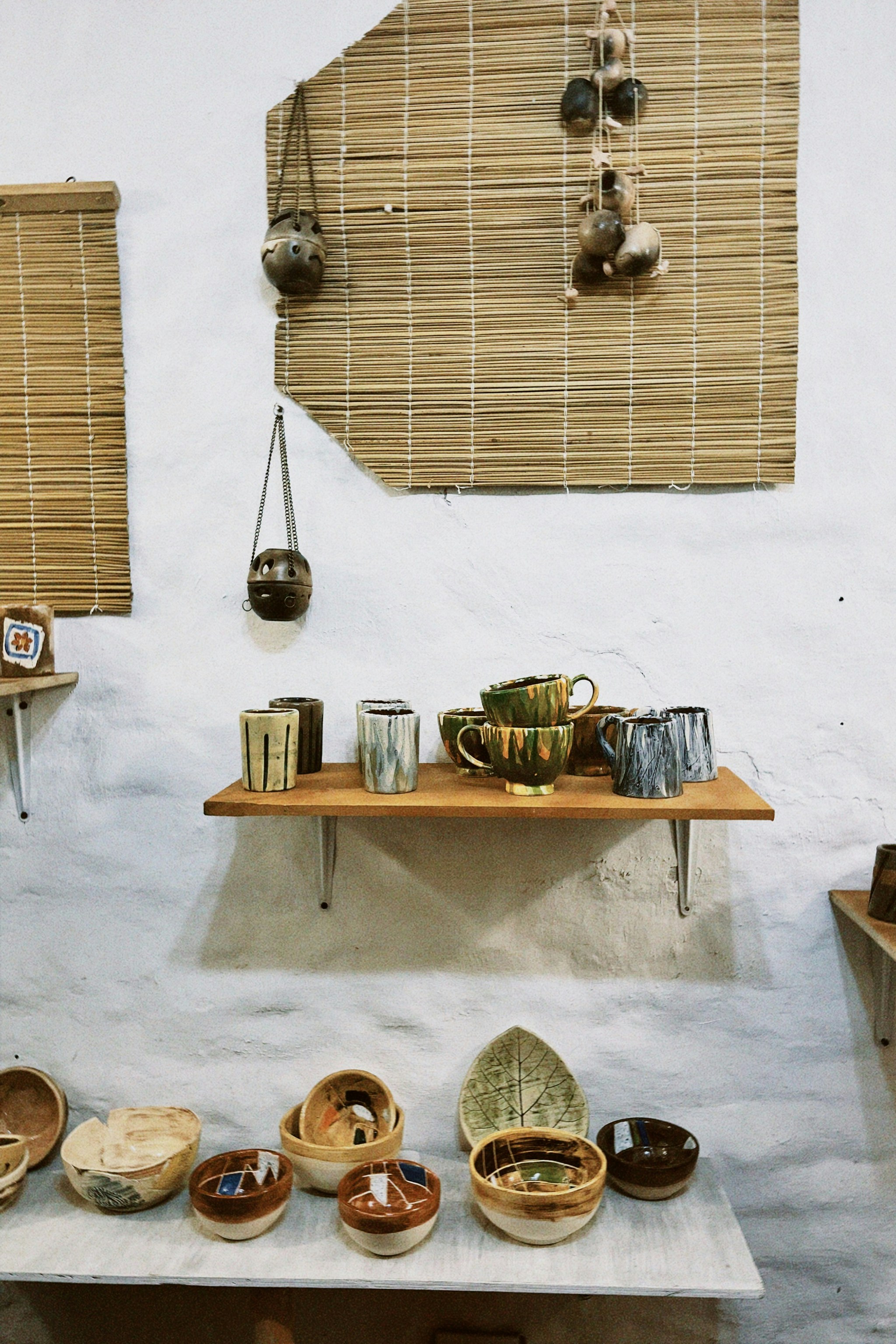 Handmade ceramic bowls and mugs arranged on a light wooden shelf in soft daylight