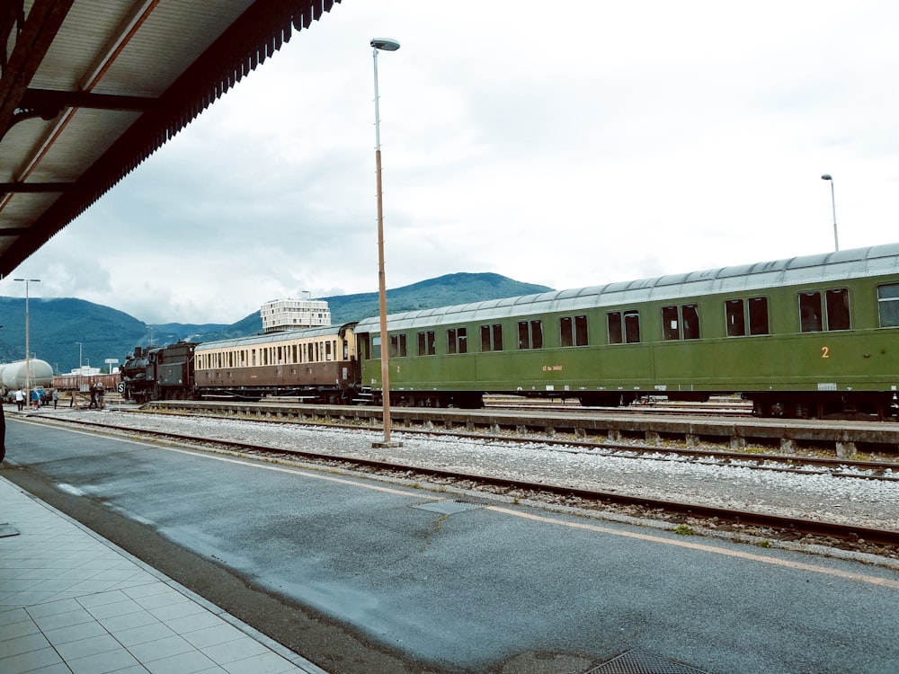 a green train traveling down train tracks next to a train station