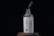 A glass bottle labeled 'SKINKRAFT LABORATORIES' stands on a wooden surface. Above the bottle, a dropper releases a droplet of liquid into the open neck. The label features a blue design of rosemary and mentions 'Rosemary with Caffeine Pro-Growth Hair Serum' in white and blue colors.