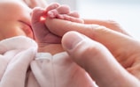 A close-up of a parent's hand holding a newborn's tiny hand, symbolizing protection.