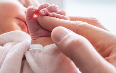 A close-up of a parent's hand holding a newborn's tiny hand, symbolizing protection.