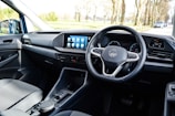 The interior of a car with a focus on the driver's area, featuring a modern steering wheel with a logo in the center, a sleek dashboard with a digital display showing several app icons, and minimalistic controls.