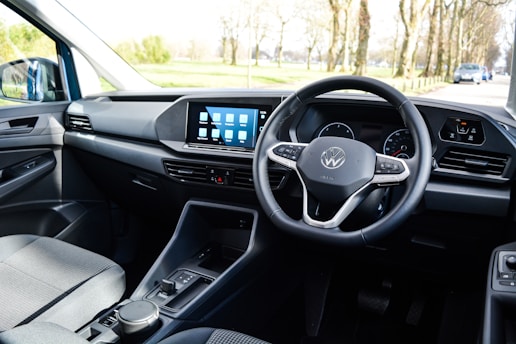 The interior of a car with a focus on the driver's area, featuring a modern steering wheel with a logo in the center, a sleek dashboard with a digital display showing several app icons, and minimalistic controls.