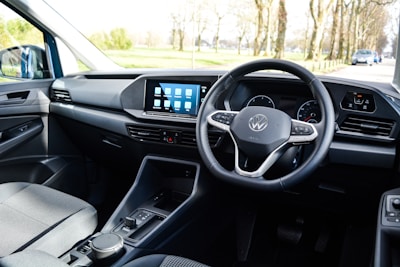 The interior of a car with a focus on the driver's area, featuring a modern steering wheel with a logo in the center, a sleek dashboard with a digital display showing several app icons, and minimalistic controls.