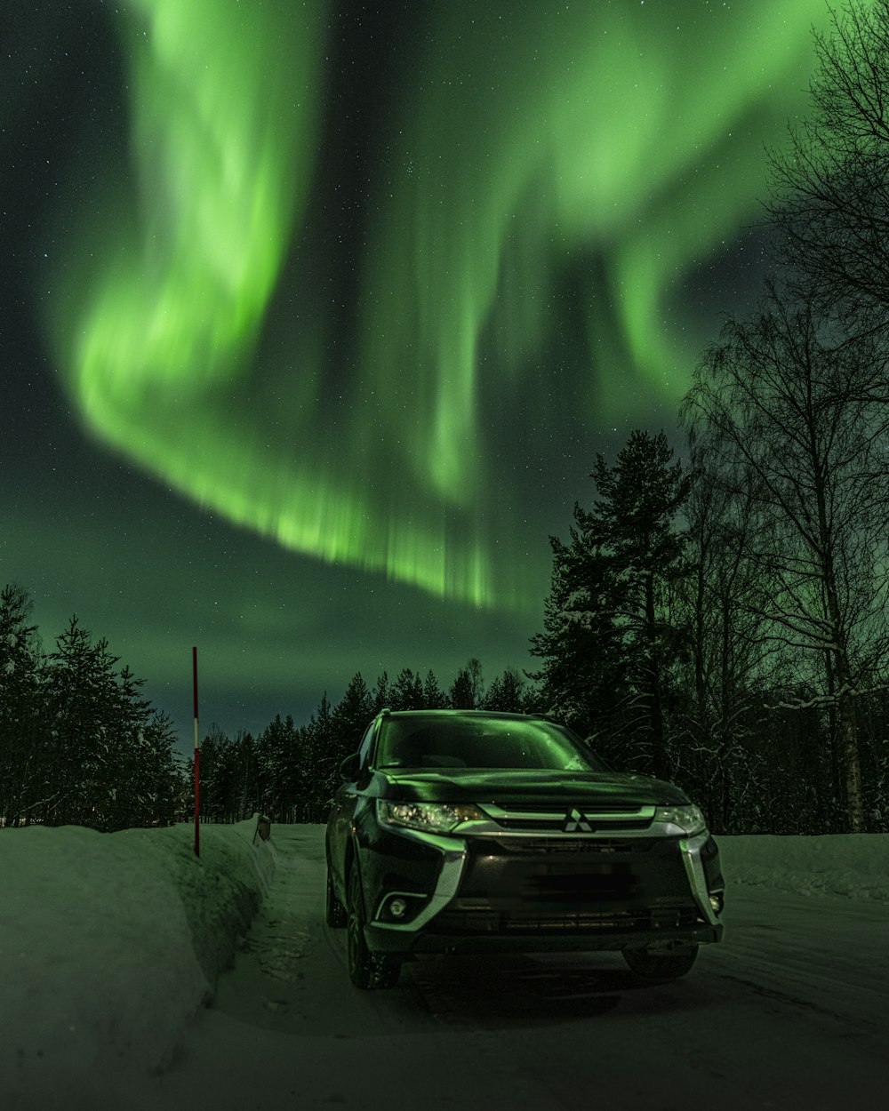 a car parked in the snow under a green aurora bore