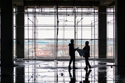 A project manager reviewing blueprints on a construction site with workers in the background.