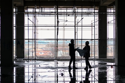 A project manager reviewing blueprints on a construction site with workers in the background.