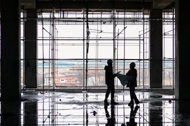 Architect reviewing blueprints on a construction site with workers in the background.