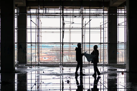 Engineers reviewing blueprints on an infrastructure project with steel frameworks in the background.