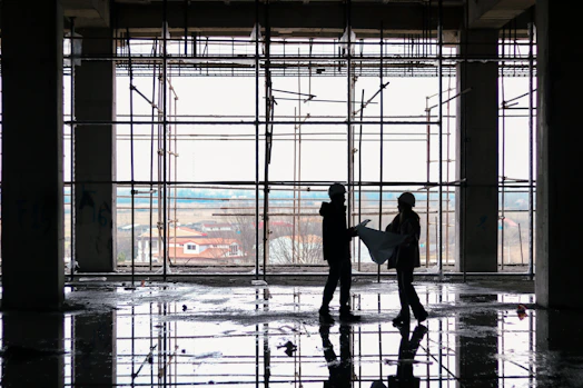 Construction workers collaborating on blueprints at a building site during daytime.