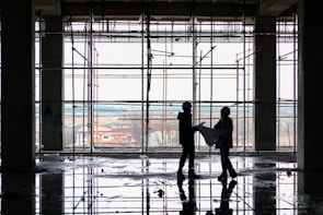 Engineers in hard hats reviewing blueprints on a busy construction site.