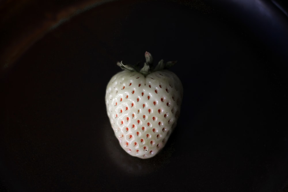 a white strawberry sitting on top of a black plate