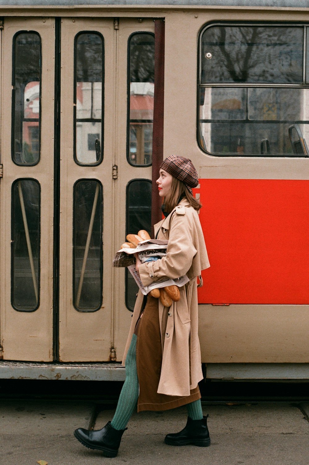 a woman in a trench coat walking past a train