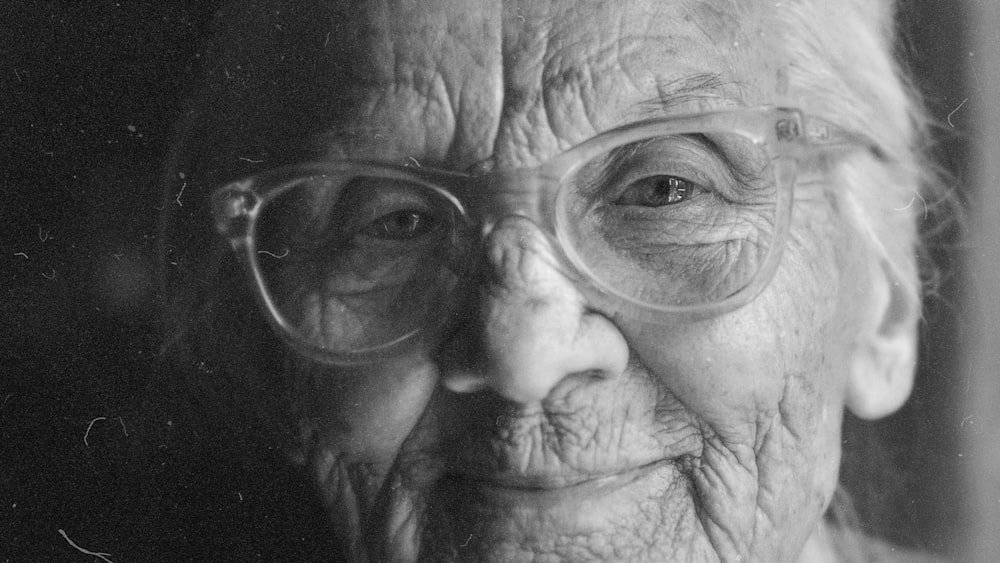 a black and white photo of an old woman with glasses