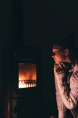 A warm, minimalistic black and gray sweater draped over a wooden chair by a glowing fireplace.