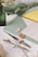 A collection of stationery items including envelopes, wax seals, and a letter opener are arranged on a surface. The scene is accented with greenery and delicate flowers in a green glass vase. The envelopes are pastel shades of mint and pink, and there is a bright yellow card peeking out. The wax seals are ornate, featuring floral designs.
