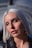 A close-up portrait of a person with platinum blonde hair, soft makeup, and a neutral expression, captured in soft lighting with a blurred background.