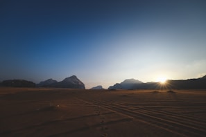 Close-up of footprints in the sand leading towards a dramatic mountain backdrop.