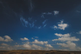 A panoramic view of a vast wind farm under a bright blue sky, turbines spinning steadily.