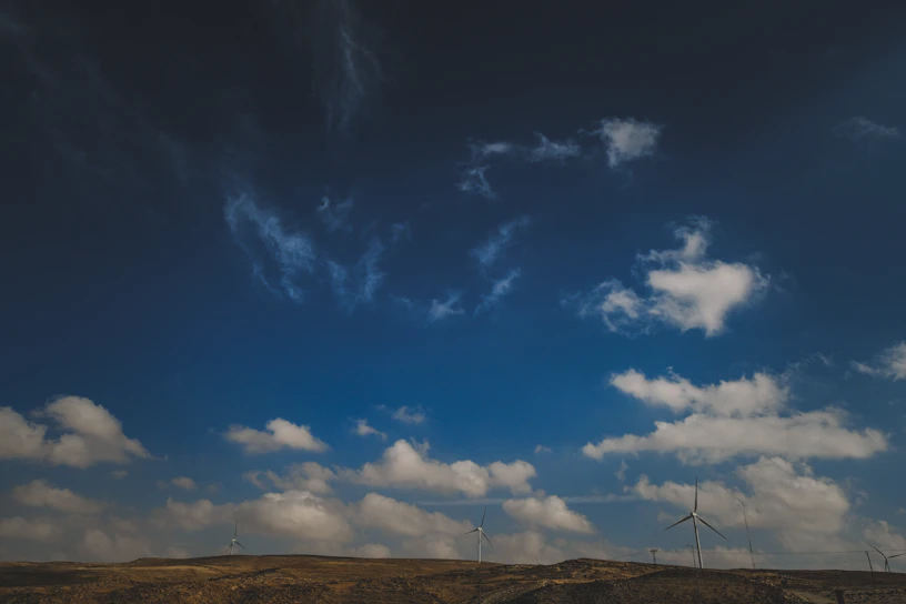 A panoramic view of a vast wind farm under a bright blue sky, turbines spinning steadily.