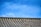 A traditional tiled roof with evenly spaced ridges sits under a clear blue sky. The roof tiles have a weathered texture, suggesting age and durability.