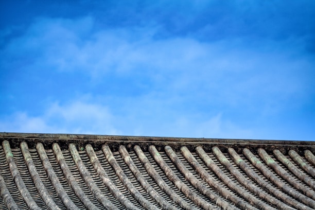 A skilled roofer installing traditional clay tiles on a residential roof under clear skies.
