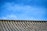 A traditional tiled roof with evenly spaced ridges sits under a clear blue sky. The roof tiles have a weathered texture, suggesting age and durability.