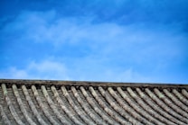 A traditional tiled roof with evenly spaced ridges sits under a clear blue sky. The roof tiles have a weathered texture, suggesting age and durability.