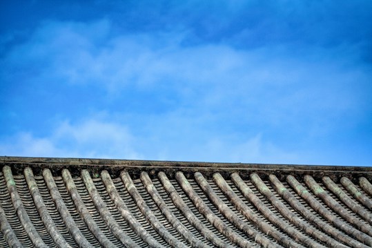 A traditional tiled roof with evenly spaced ridges sits under a clear blue sky. The roof tiles have a weathered texture, suggesting age and durability.