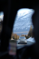 A rugged SUV cruising along a scenic mountain road surrounded by pine trees.
