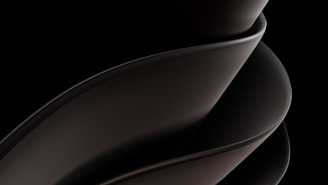 A sleek, smooth, and abstract form consisting of overlapping curved surfaces, primarily in dark tones and gradients. The design is fluid and modern, suggesting movement and elegance.