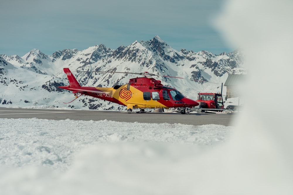 a red and yellow helicopter sitting on top of a snow covered mountain