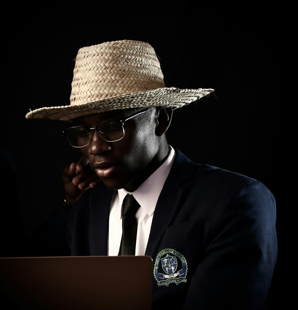 a man in a suit and hat using a laptop