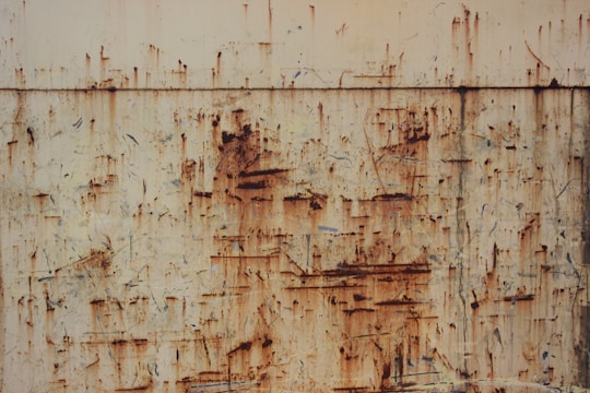 A weathered and rusted metal surface exhibits various shades of orange and brown, with visible texture, scratches, and corrosion patterns throughout.