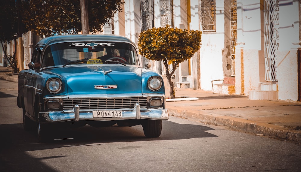 a blue car driving down a street next to tall buildings