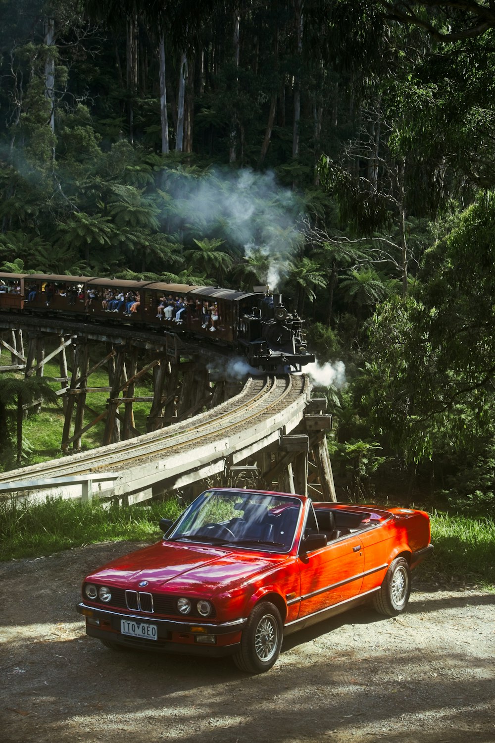 a red car parked next to a train on a track