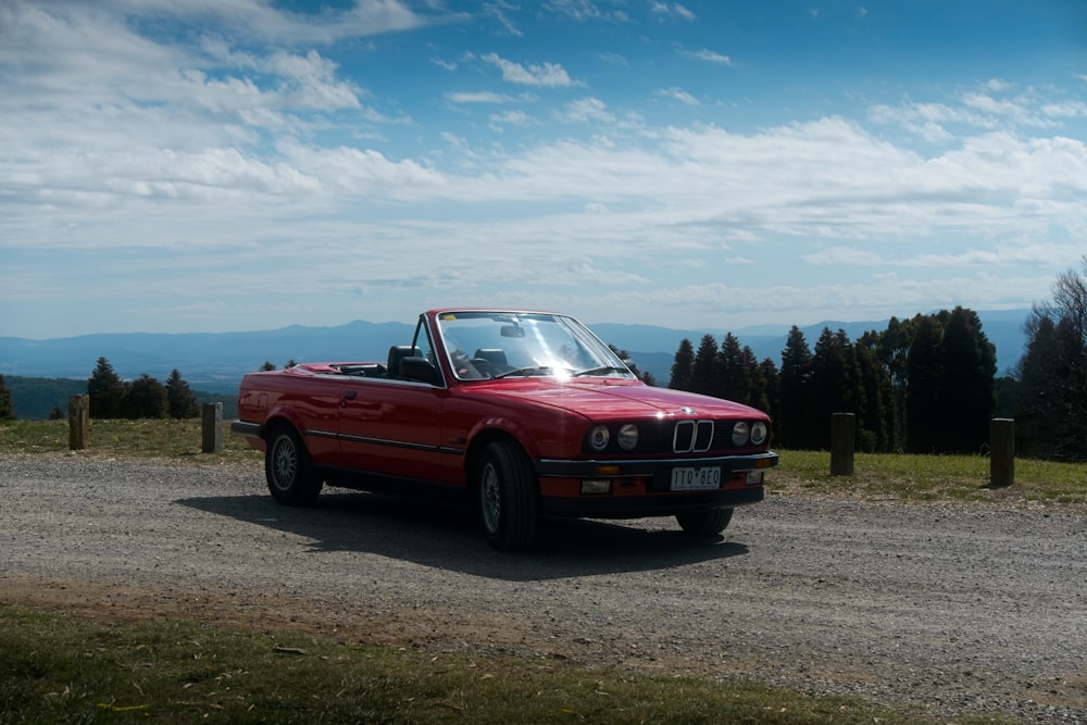 a red convertible car parked on a gravel road