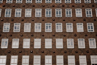 A building facade with a grid pattern of white-framed windows against a textured brick wall. Decorative round ceramic elements are interspersed between the windows, creating a diagonal pattern.