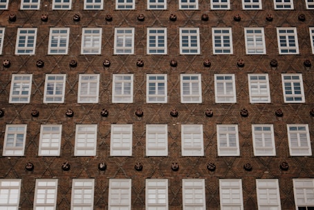 A building facade with a grid pattern of white-framed windows against a textured brick wall. Decorative round ceramic elements are interspersed between the windows, creating a diagonal pattern.